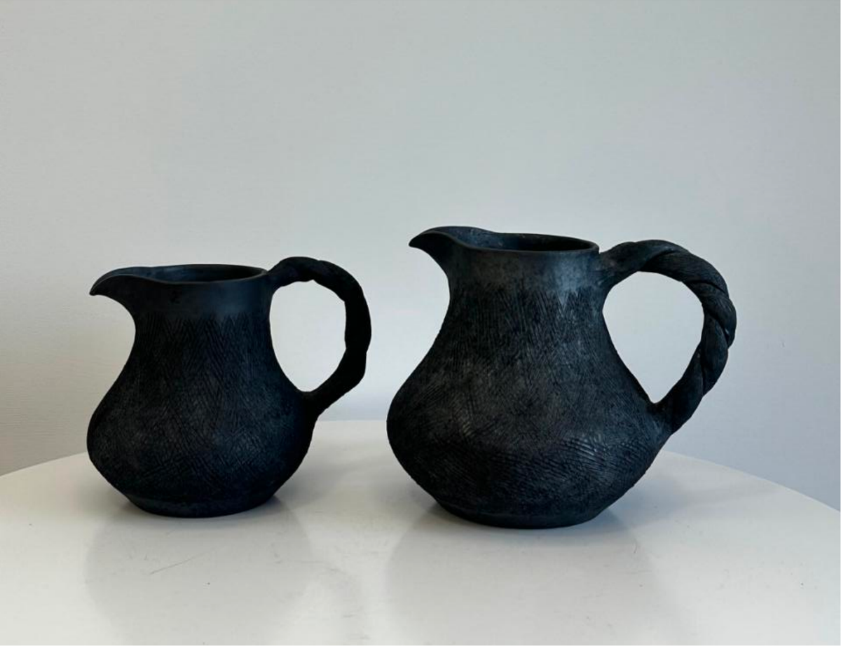 Two Tibetan black pottery sharing pitchers with rounded bodies, pouring spouts and loop handles on a light surface.